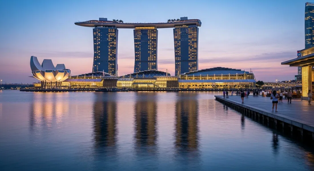 Marina Bay Sands al atardecer, tres torres iluminadas elevándose detrás de la bahía con el SkyPark uniendo la parte superior y reflejos brillando en el agua